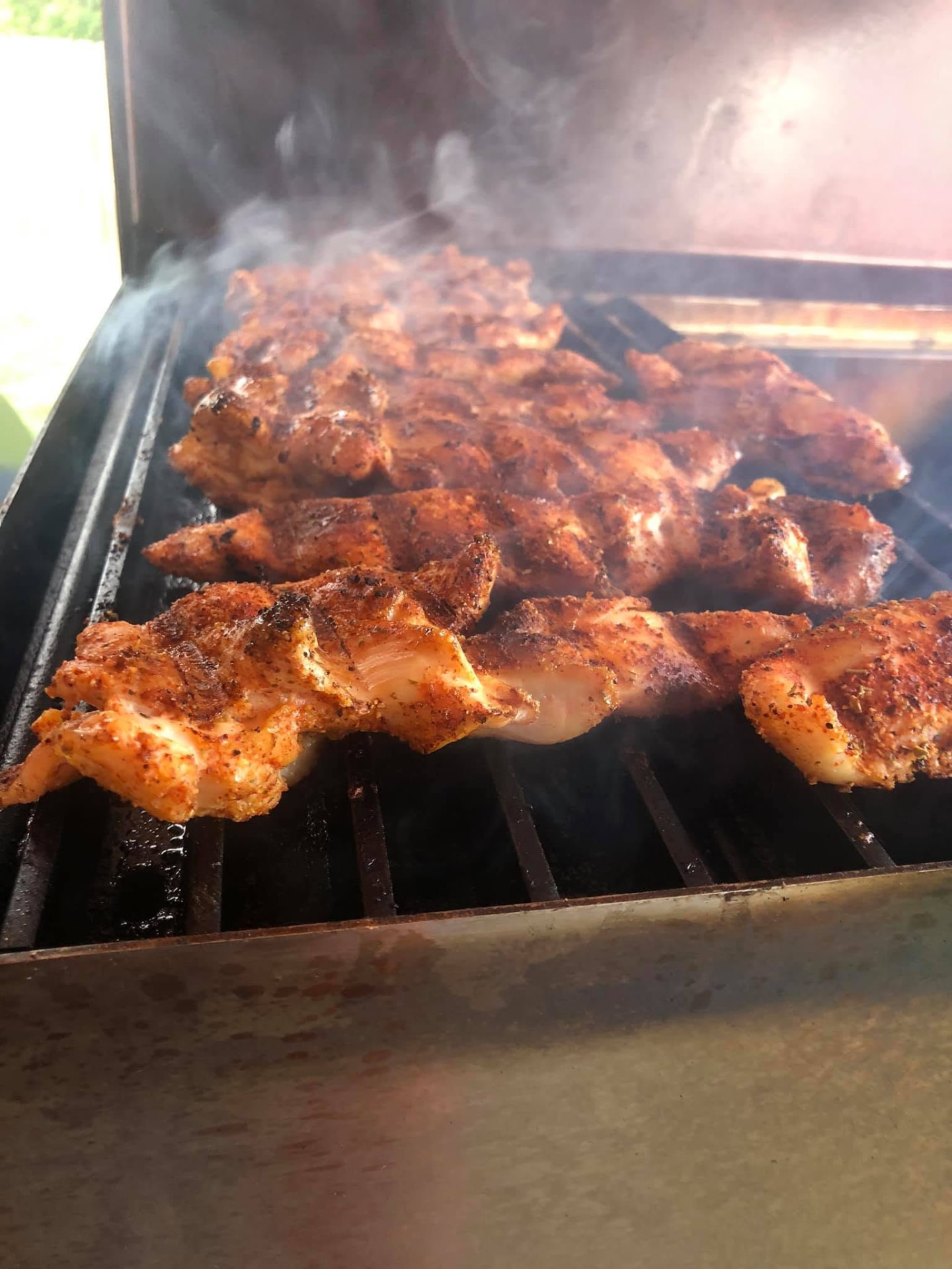Seasoned chicken smoking on the grill